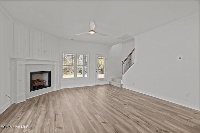 unfurnished living room featuring light wood-style floors, ornamental molding, a brick fireplace, ceiling fan, and stairs