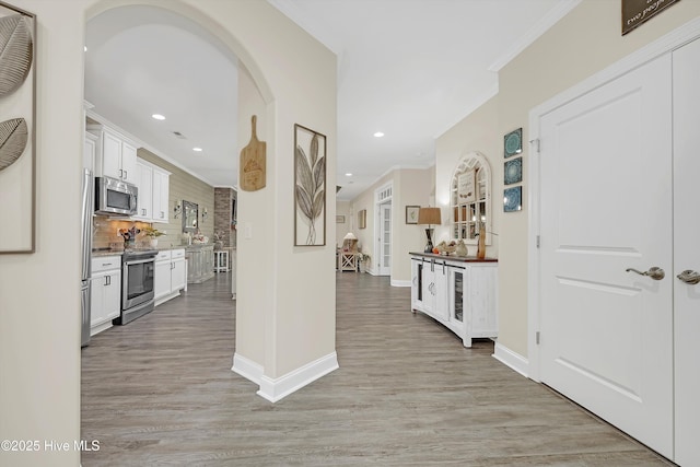 interior space with white cabinetry, crown molding, light wood-type flooring, stainless steel appliances, and backsplash