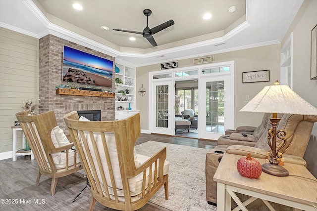 sitting room featuring hardwood / wood-style floors, a fireplace, ornamental molding, french doors, and a raised ceiling