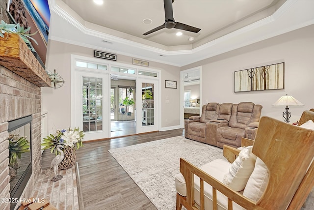 living room featuring a fireplace, a tray ceiling, wood-type flooring, and ornamental molding