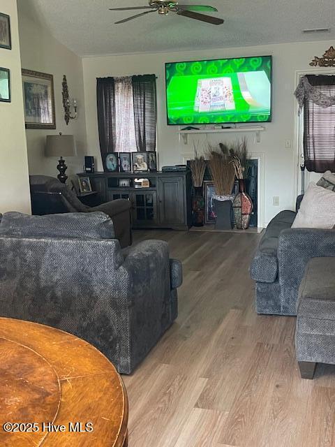 living room with vaulted ceiling, ceiling fan, hardwood / wood-style floors, and a textured ceiling