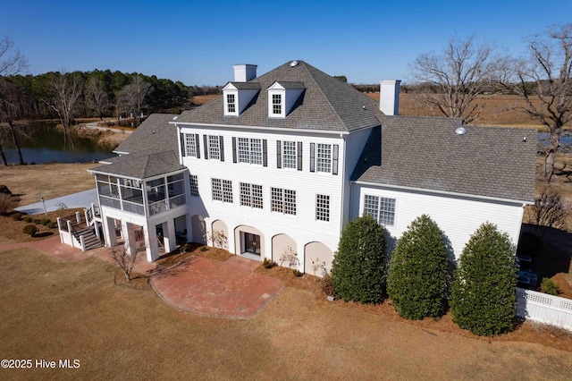 back of house with a water view, a sunroom, a lawn, and a patio area