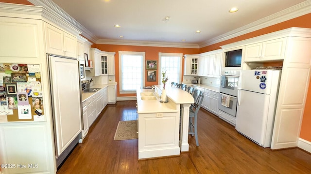 kitchen with white appliances, white cabinetry, ornamental molding, a kitchen island, and dark hardwood / wood-style flooring