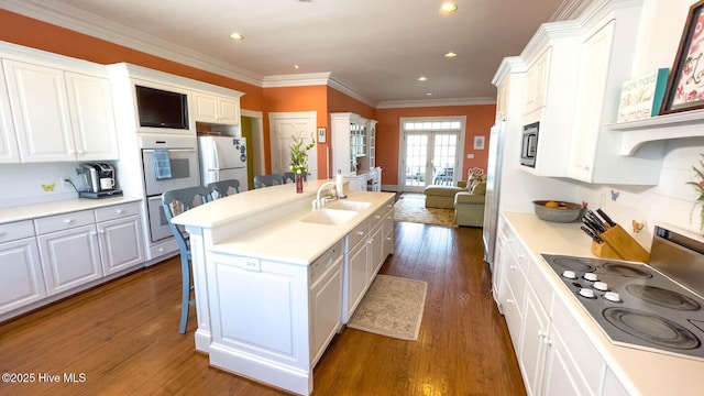 kitchen with sink, stovetop, white cabinetry, a center island with sink, and white fridge