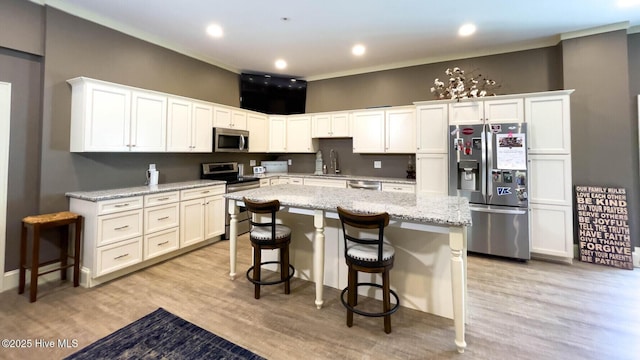 kitchen with light stone counters, stainless steel appliances, white cabinets, and a kitchen bar