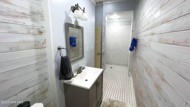 bathroom with wood walls, vanity, and a tile shower