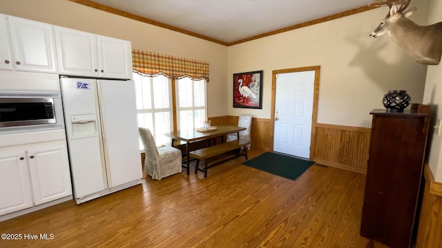 kitchen featuring white cabinetry, crown molding, light hardwood / wood-style flooring, stainless steel microwave, and white refrigerator with ice dispenser