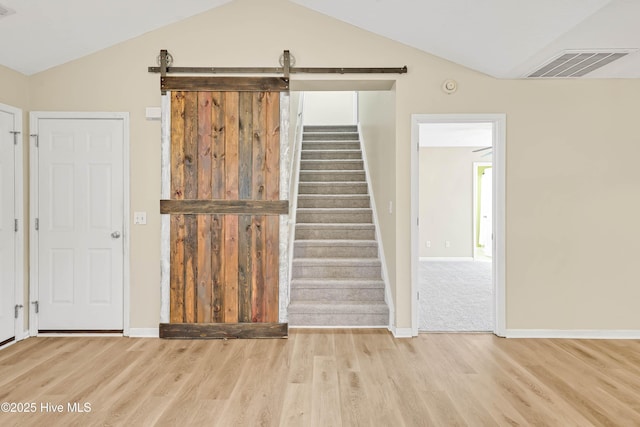 stairs featuring visible vents, wood finished floors, a barn door, and vaulted ceiling