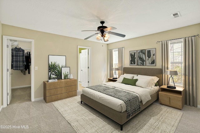 bedroom featuring a walk in closet, multiple windows, light colored carpet, and visible vents