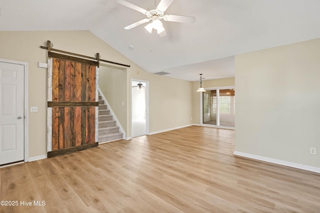 unfurnished room featuring a barn door, light wood-style floors, ceiling fan, and vaulted ceiling