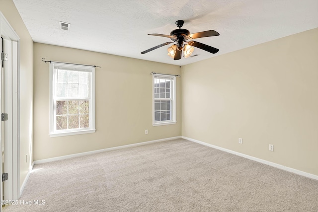 carpeted spare room with a wealth of natural light, visible vents, a textured ceiling, and a ceiling fan