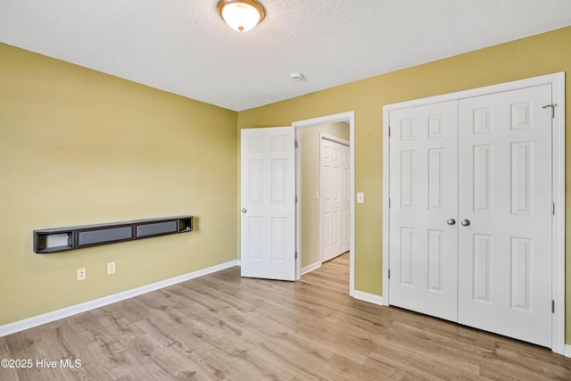 unfurnished bedroom with a closet, a textured ceiling, baseboards, and wood finished floors