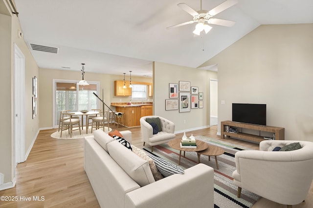 living room with a ceiling fan, visible vents, light wood finished floors, baseboards, and vaulted ceiling