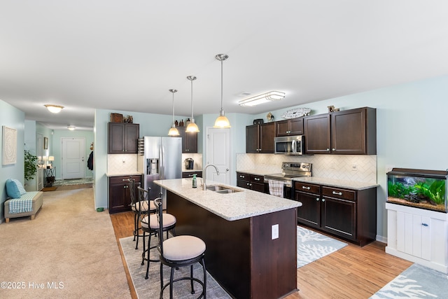 kitchen featuring dark brown cabinetry, a breakfast bar, a sink, appliances with stainless steel finishes, and tasteful backsplash