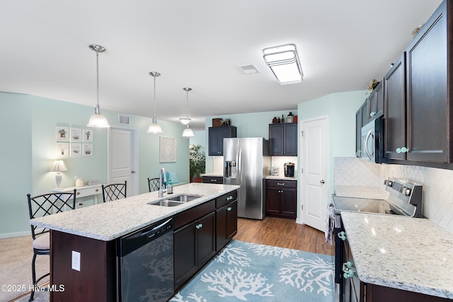 kitchen featuring visible vents, decorative backsplash, an island with sink, stainless steel appliances, and a sink