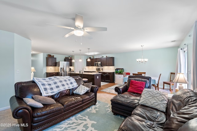 living area featuring baseboards, light colored carpet, and ceiling fan with notable chandelier