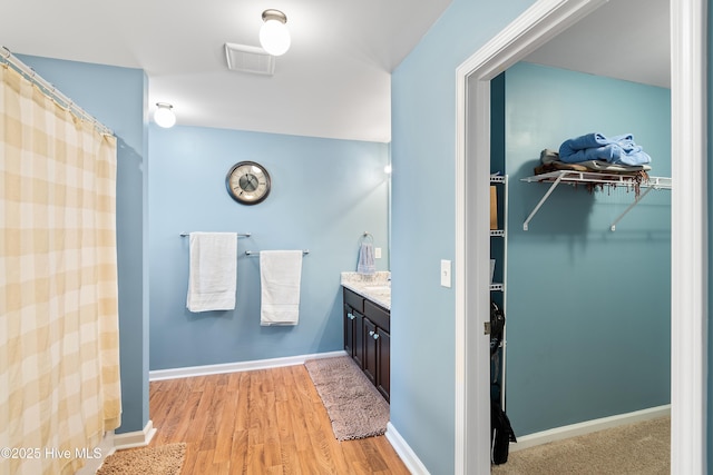 full bathroom featuring baseboards, visible vents, wood finished floors, a spacious closet, and vanity