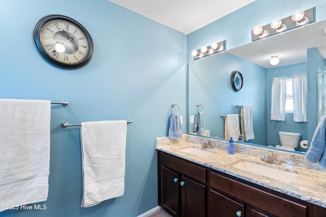 bathroom with double vanity, a sink, and toilet