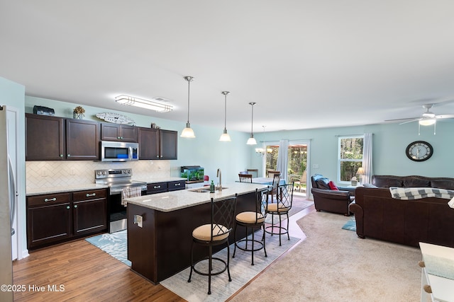 kitchen with appliances with stainless steel finishes, open floor plan, dark brown cabinetry, a sink, and a kitchen breakfast bar