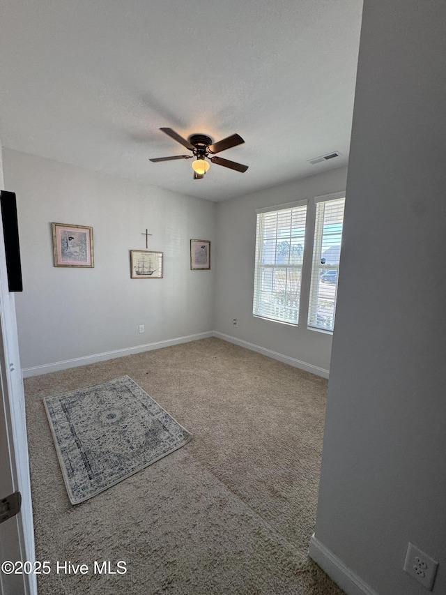 carpeted empty room with baseboards, visible vents, and a ceiling fan