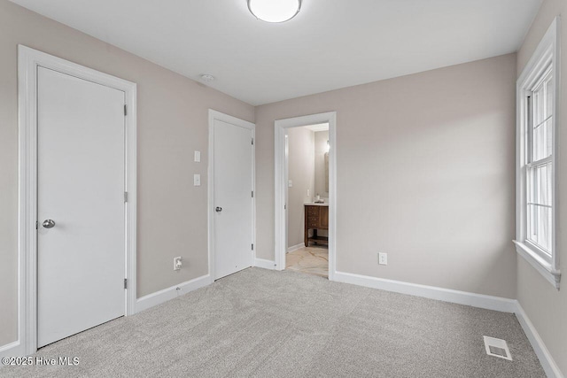 unfurnished bedroom featuring light colored carpet and ensuite bath