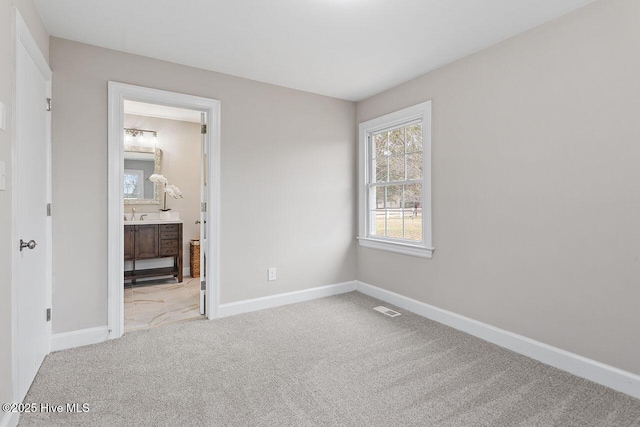 unfurnished bedroom featuring light colored carpet and ensuite bathroom