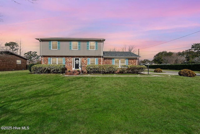 colonial inspired home featuring a yard and brick siding