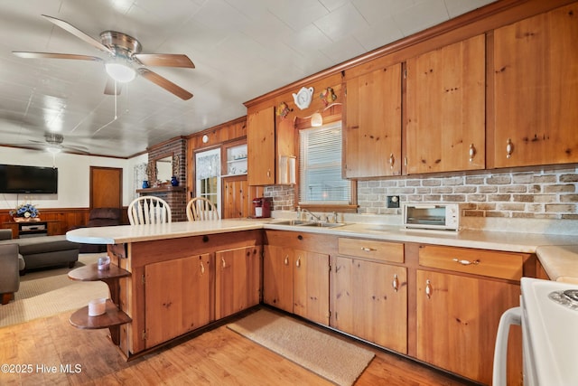 kitchen with sink, kitchen peninsula, ceiling fan, light hardwood / wood-style floors, and stove