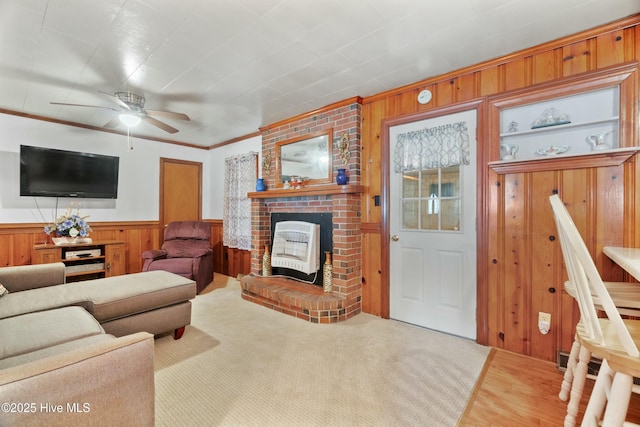 living room featuring hardwood / wood-style floors, wooden walls, a fireplace, ceiling fan, and crown molding