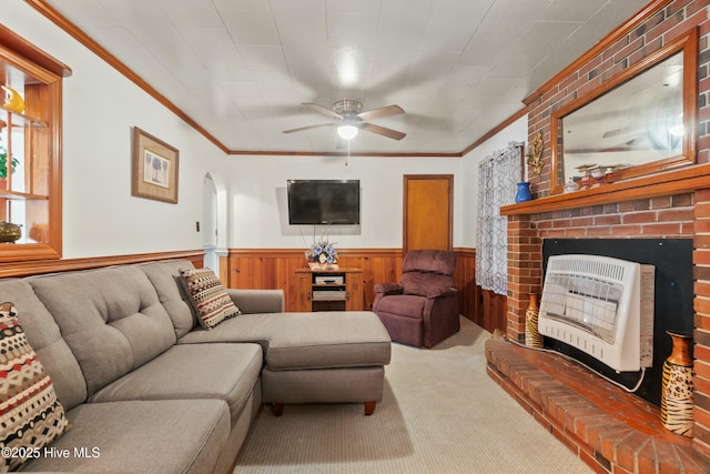 carpeted living room with heating unit, a brick fireplace, ornamental molding, and ceiling fan