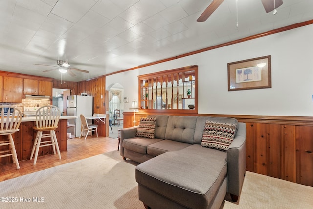 living room featuring crown molding, wooden walls, ceiling fan, and light wood-type flooring