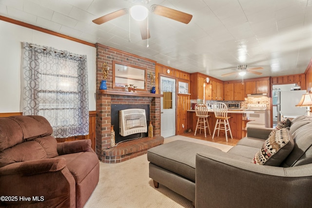 carpeted living room with a brick fireplace, crown molding, wooden walls, and ceiling fan