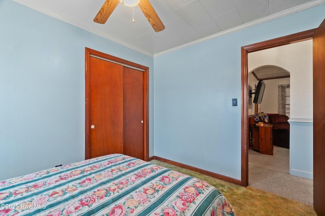 carpeted bedroom featuring ornamental molding, a closet, and ceiling fan