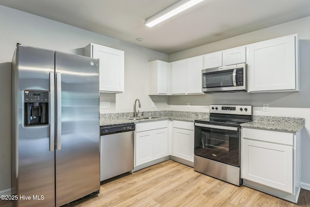 kitchen featuring sink, appliances with stainless steel finishes, light stone counters, white cabinets, and light wood-type flooring