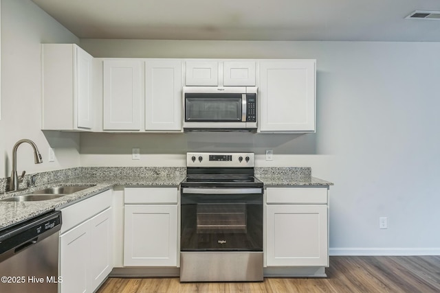 kitchen with sink, white cabinetry, stainless steel appliances, light stone counters, and light hardwood / wood-style floors