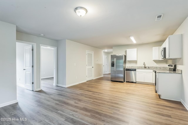 kitchen with appliances with stainless steel finishes, sink, white cabinets, and light hardwood / wood-style floors