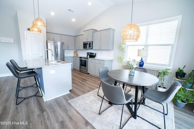 kitchen featuring an island with sink, appliances with stainless steel finishes, gray cabinetry, and pendant lighting