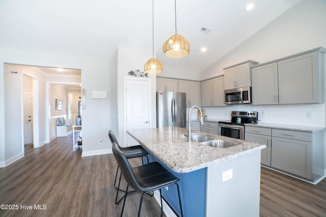 kitchen featuring light stone counters, stainless steel appliances, an island with sink, and pendant lighting