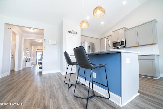 kitchen featuring pendant lighting, wood-type flooring, gray cabinetry, backsplash, and stainless steel appliances