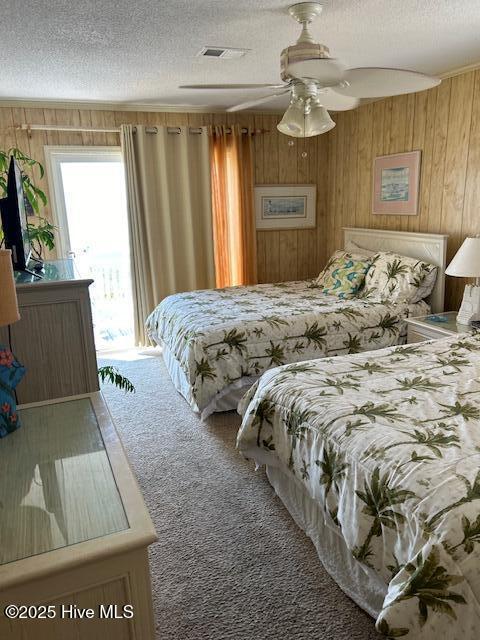 carpeted bedroom featuring visible vents, ceiling fan, access to exterior, a textured ceiling, and wood walls