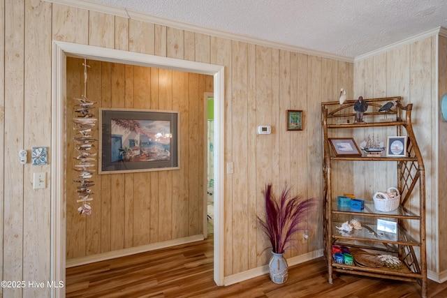 hall with a textured ceiling, baseboards, wood finished floors, crown molding, and wooden walls