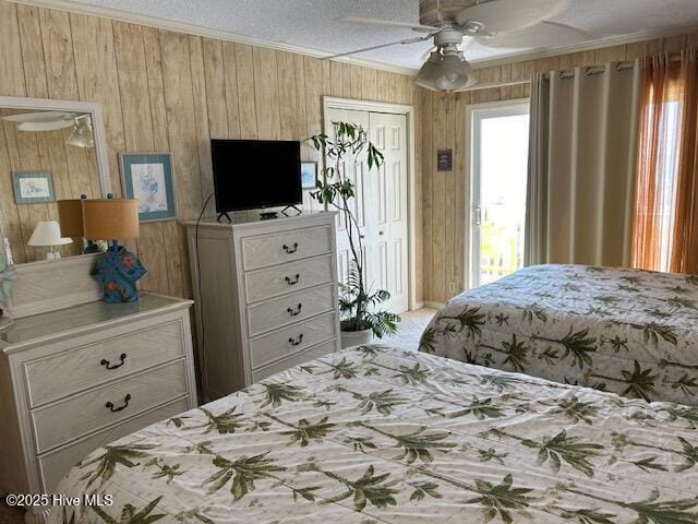 carpeted bedroom featuring a textured ceiling, wood walls, a ceiling fan, ornamental molding, and a closet