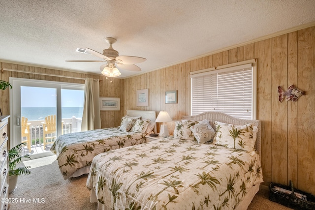 carpeted bedroom with a textured ceiling, ornamental molding, access to outside, and wood walls