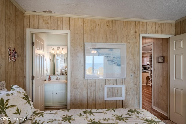 bedroom with wood finished floors, ornamental molding, a sink, ensuite bath, and a textured ceiling