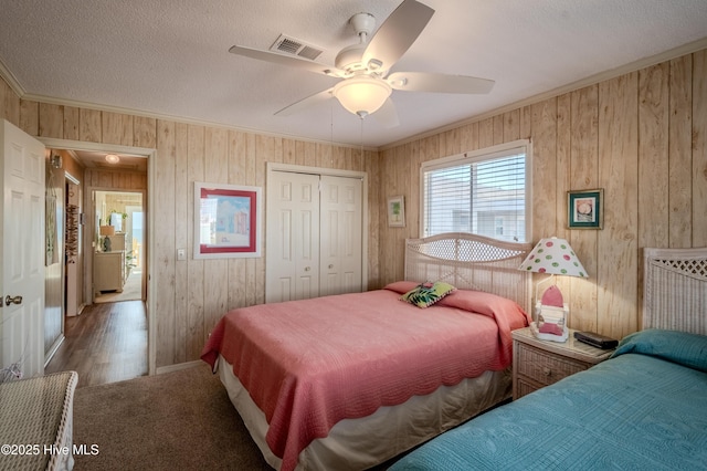 bedroom with a closet, wood walls, ornamental molding, and visible vents