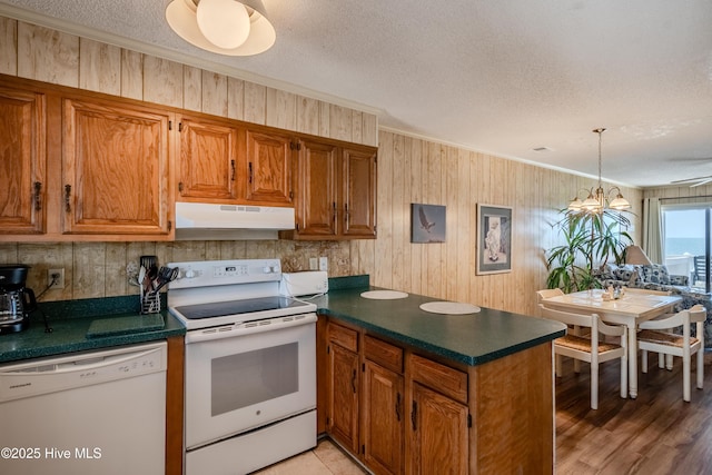 kitchen with under cabinet range hood, dark countertops, white appliances, a peninsula, and a textured ceiling