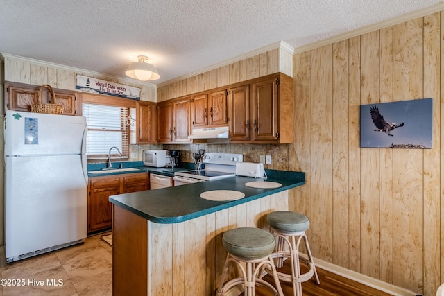 kitchen featuring a sink, dark countertops, white appliances, brown cabinets, and under cabinet range hood