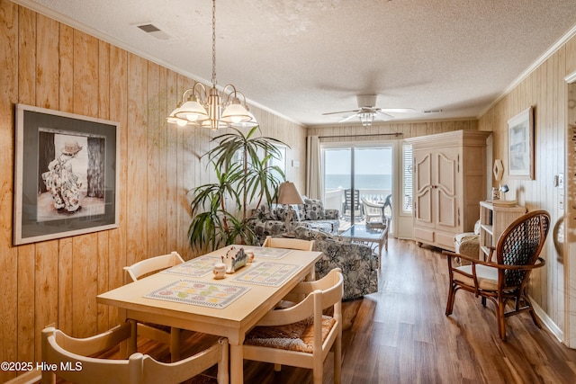 dining area featuring wooden walls, wood finished floors, crown molding, a textured ceiling, and ceiling fan with notable chandelier