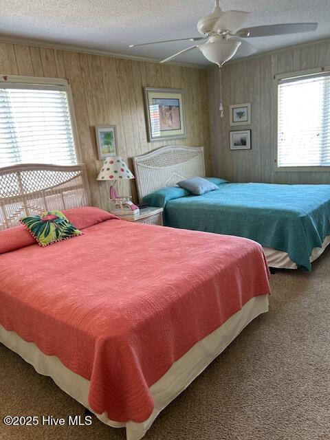 bedroom with wood walls, ceiling fan, a textured ceiling, and carpet flooring