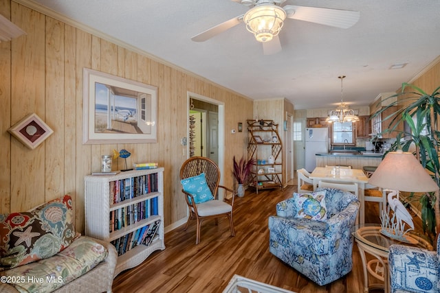 living area with ceiling fan with notable chandelier, wood finished floors, wood walls, and crown molding